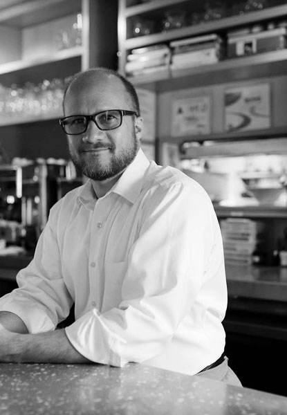 smiling chef with glasses leaning over bar counter